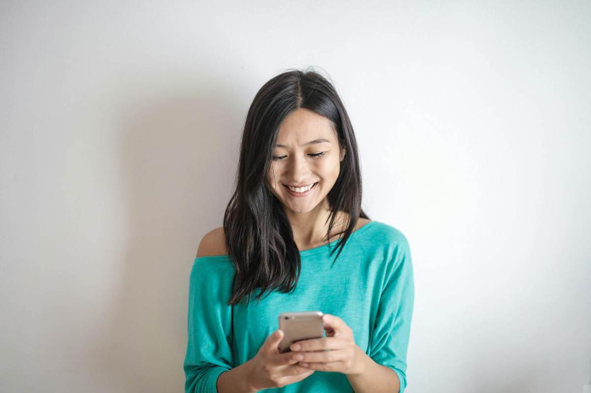 Person texting on phone with a smile, representing creator-fan chat conversation